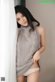 A woman in a gray sweater leaning against a curtain.