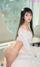 A woman in a white sweater and panties sitting on a bed.