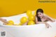 A woman laying in a bathtub with yellow balloons.