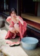 A woman in a red kimono eating a slice of watermelon.