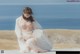 A woman in a white dress sitting on a wooden dock by the ocean.